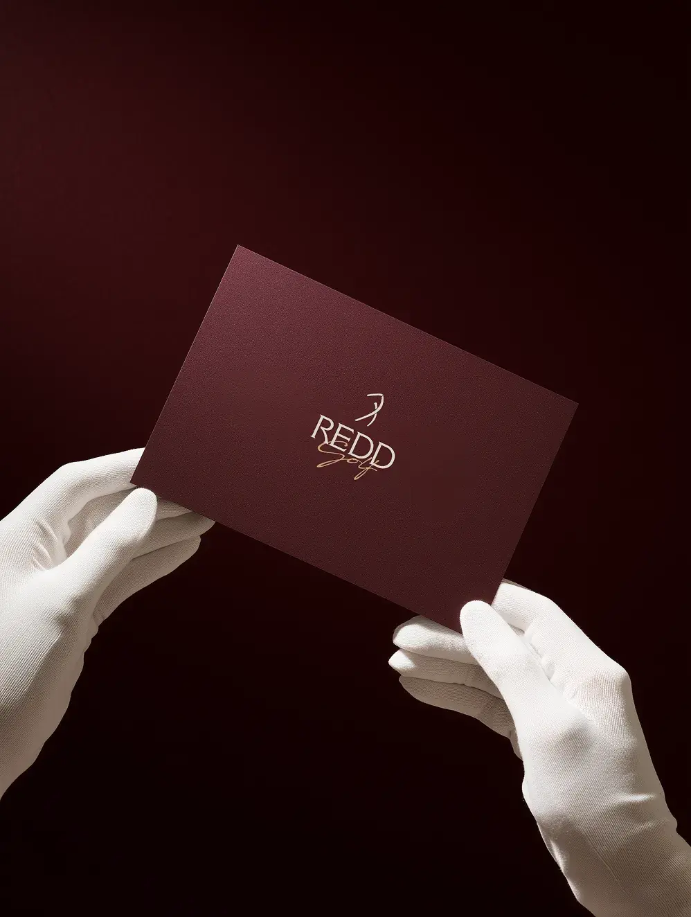 Gloved hands holding a maroon Redd Golf card with the gold logo