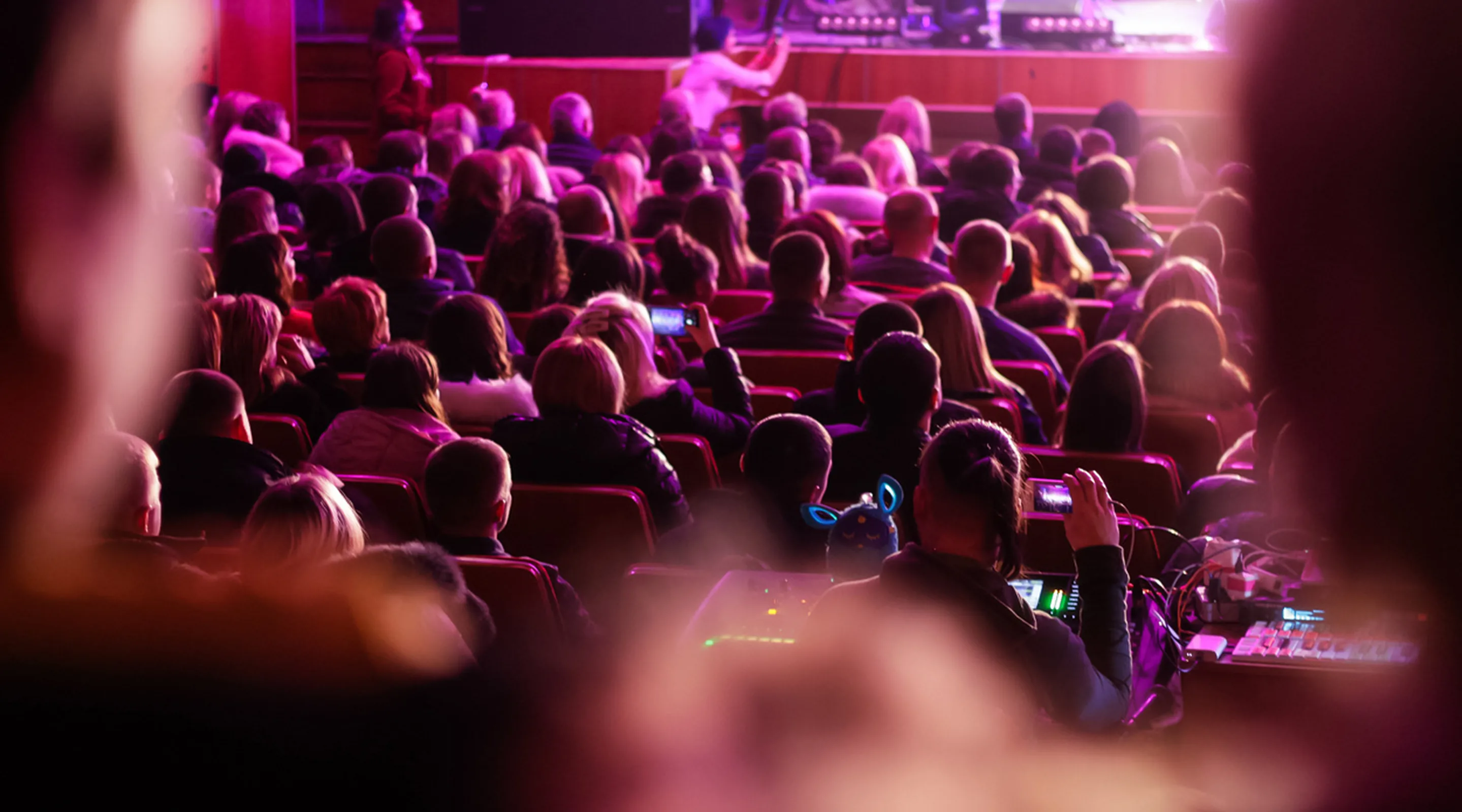 Audience in a theater washed in magenta light