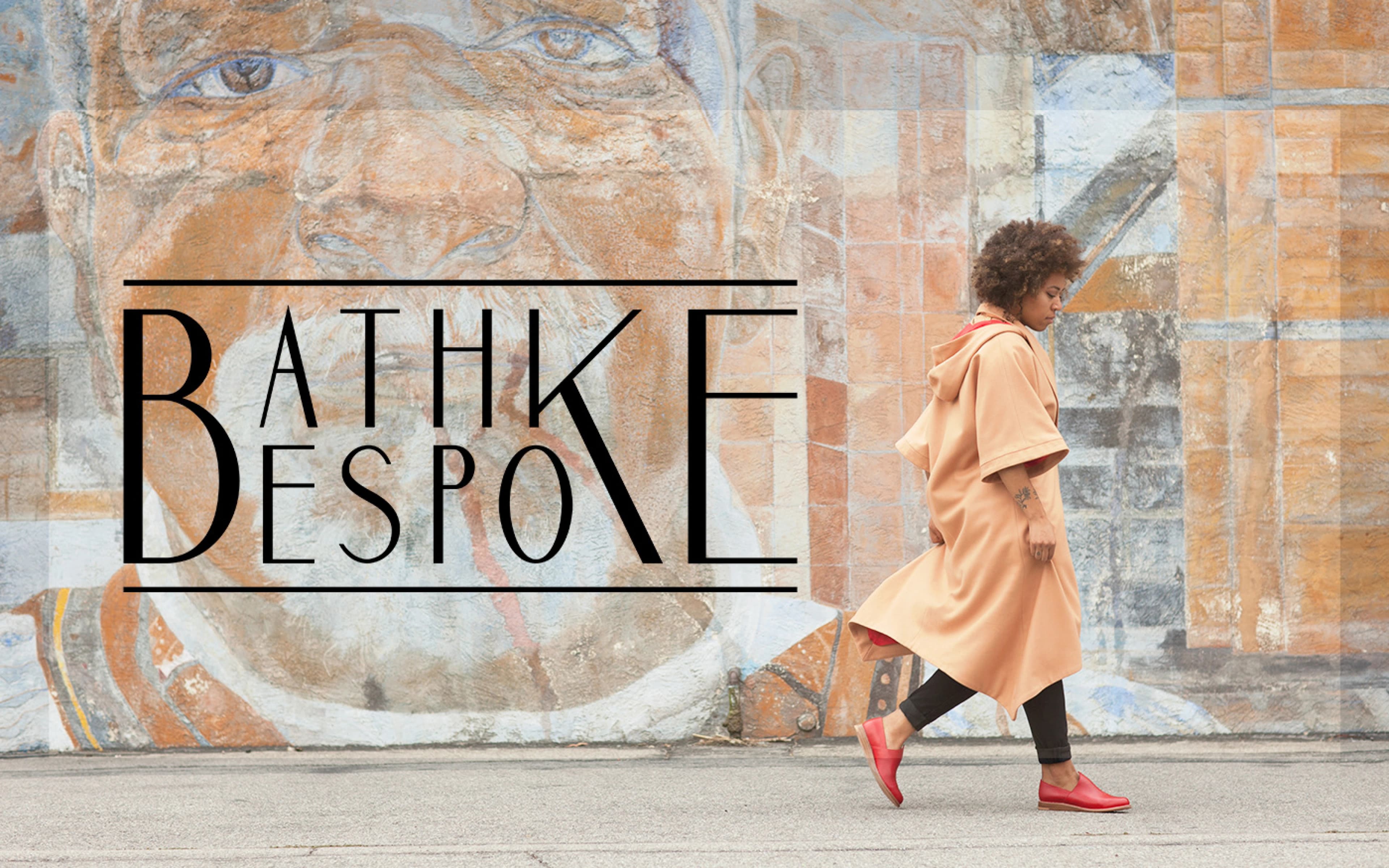 Bathke Bespoke campaign photograph: model in a camel coat and red bespoke shoes walking past a painted mural
