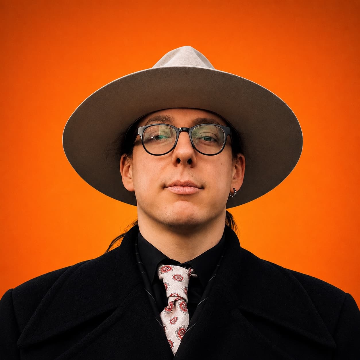 Portrait of Vanja Stojanović, creative director of The Shadow Legacy, in a wide-brim hat against an orange backdrop
