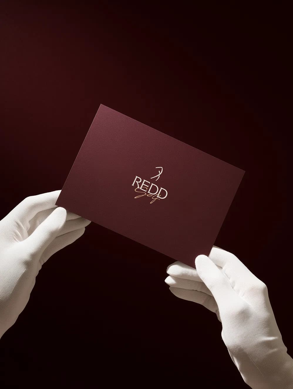 Gloved hands holding a maroon Redd Golf card with the gold logo